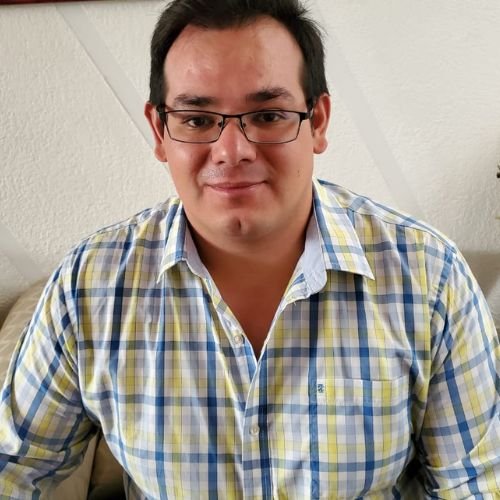 el psicólogo Alan Guarneros siendo el una persona con viendo hacia el frente con una camisa con lineas de color azul amarillas creando cuadros, en la cara porta unos lentes de color negro y se le ve sonriendo.